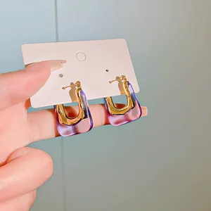 Detailed close-up of U-shaped hoop earrings featuring gold metal and purple resin.