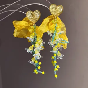 Dettaglio di orecchini a cuore giallo con fiori di chiffon e nappe di perline colorate