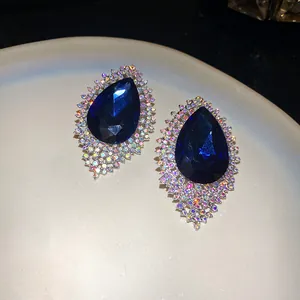 Close-up of oversized blue waterdrop stud earrings with iridescent rhinestone halo.