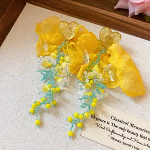 Dettaglio orecchini a nappa con fiori in chiffon giallo e perni a cuore stile resort.