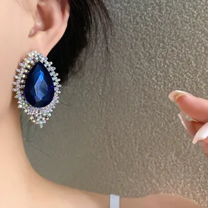 Close-up detail of oversized blue teardrop earring with rhinestone border on ear
