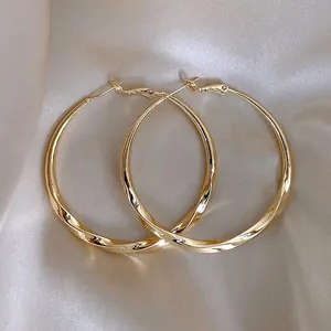 Detailed view of elegant gold-toned twisted hoop earrings on champagne satin background