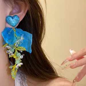 Dettaglio degli orecchini con nappine in chiffon a cuore blu indossati all'orecchio