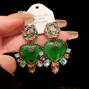 Close-up of vintage palace style green heart earrings with colorful teardrop gems.
