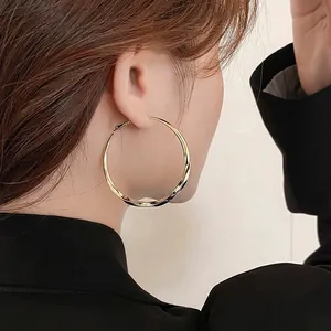 Detail view of large gold twisted hoop earrings worn by a model for a stylish look.