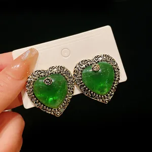Detail of vintage palace style heart-shaped earrings with green stone and silver floral border.