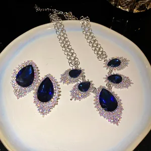 Detail view of a luxury blue waterdrop crystal necklace and earring jewelry set on a white plate.