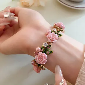 Primo piano di un braccialetto in stile pastorale con rose rosa, perle e strass su un polso.