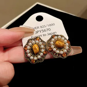 Close-up of vintage style earrings with tiger eye stone, pearls, and orange crystals.