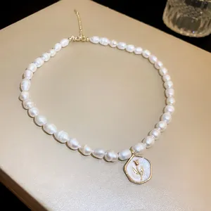 Close-up of French-style pearl necklace featuring a golden tulip pendant on cream base