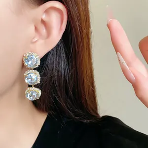 Close-up of elegant gold drop earrings with three tiered sparkling round crystals.