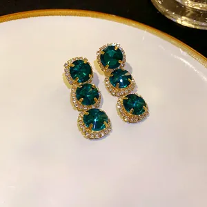 Close-up of emerald green geometric drop earrings with gold finish and rhinestones