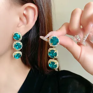 Detailed close-up of three-tier emerald green crystal drop earrings with halo setting