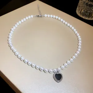 Elegant close-up of a white pearl necklace featuring a black heart-shaped pendant detail.