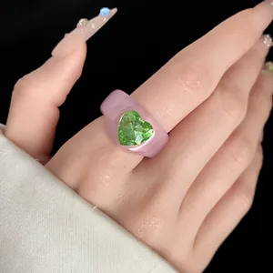 Close-up of a stylish pink resin ring featuring a green heart-shaped crystal on the finger