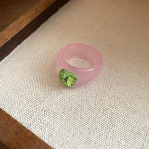 Close-up of a pink resin ring featuring a sparkling green heart-shaped gemstone.