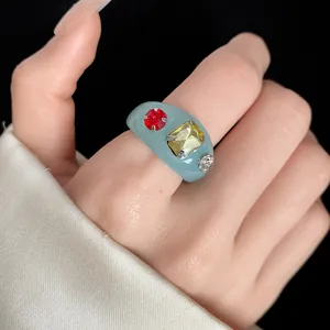 Close-up of a light blue resin ring with vibrant colorful rhinestones on a finger