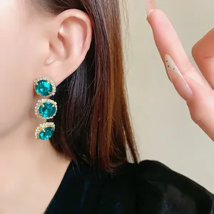 High-quality detail shot of three-tier emerald green crystal earrings worn on a model's ear