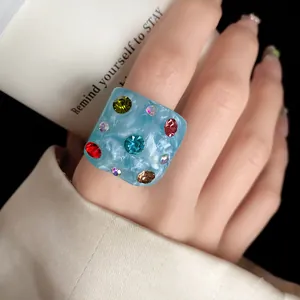 Macro detail of a chunky blue resin ring featuring vibrant multi-color rhinestones