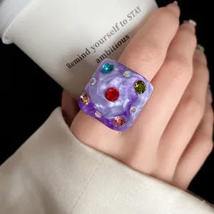 Close-up view of a purple marbled resin ring featuring colorful embedded rhinestones