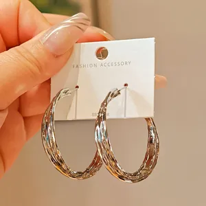 Detail view of large silver textured hoop earrings on a minimalist fashion accessory card