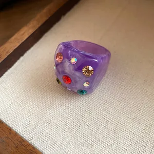 Detailed close-up view of purple resin ring featuring colorful rhinestone inlay and marble texture.
