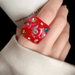 Close-up of a chunky square red resin ring with colorful sparkling rhinestones for women.
