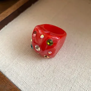 Close-up detail of a red chunky resin ring inlaid with colorful sparkling rhinestones