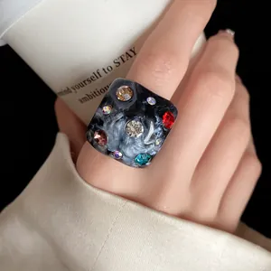 Close-up view of a chic marble resin square ring featuring colorful rhinestones on a hand