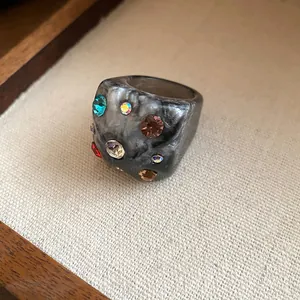 Close-up of a chunky grey marble resin ring with embedded multi-colored rhinestones.