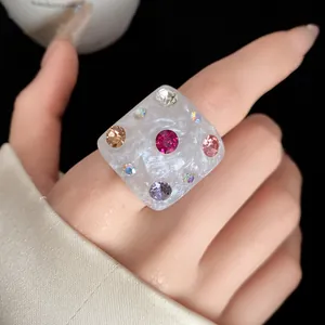Detailed view of a pearly white square resin ring decorated with colorful rhinestones