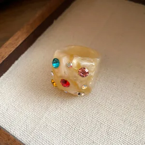 Macro detail of thick beige resin ring with multi-color rhinestones inlay