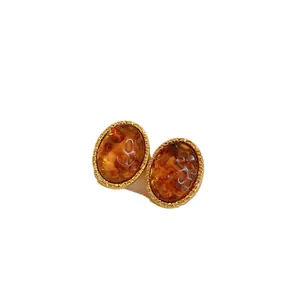 Eleganti orecchini ovali marrone Maillard con bordo dorato testurizzato.