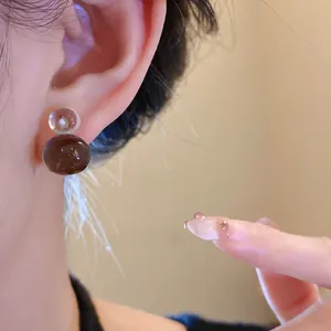 Macro detail view of transparent and brown jelly resin gourd stud earrings worn on the ear