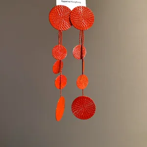 Macro shot of long red tassel earrings featuring textured circular discs and screw patterns.