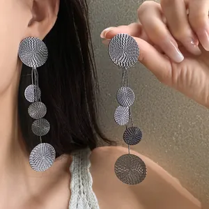 Detail of long silver needle tassel earrings with textured round grey discs.