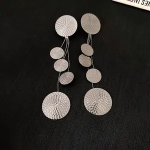 Close-up detail of silver-toned dangle earrings featuring multiple textured circular discs
