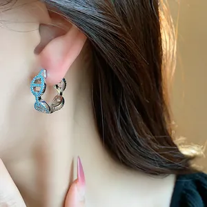Close-up detail of silver-toned anchor link hoop earrings with blue stones on a model