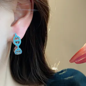 Close-up of elegant pig nose earrings with blue zircon inlays on a model's ear.