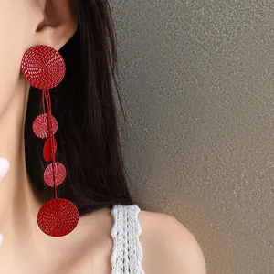 Detailed view of red spray-painted round tassel drop earrings worn by a model