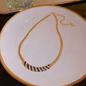 Macro detail of a gold plated curved necklace featuring black and white rhinestone stripes