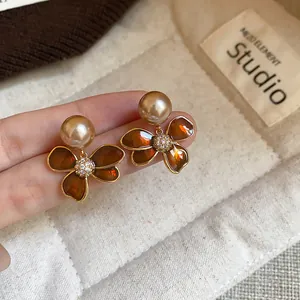 Close-up of gold-plated flower stud earrings with amber petals and champagne pearls