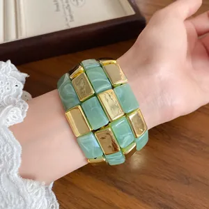 Primo piano di un bracciale in acrilico marmo verde e quadrati dorati al polso femminile