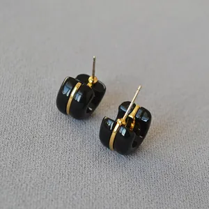 Detailed macro view of glossy black and gold chunky hoop earrings on grey fabric