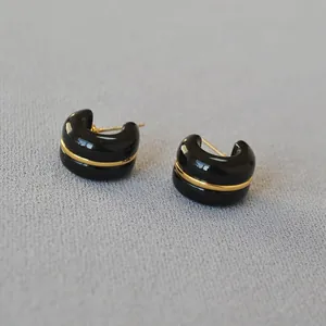 Macro detail view of minimalist black C-shaped earrings with a central gold band design