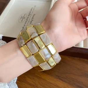Vista dettagliata di un ampio bracciale in blocchi di acrilico con texture oro e marmo al polso