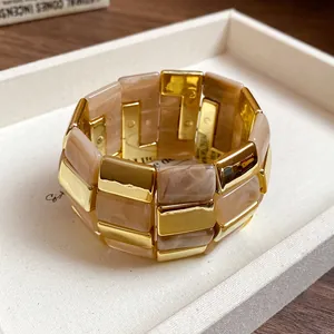 Dettaglio ravvicinato del bracciale in acrilico marmorizzato e maglie dorate.