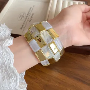 Primo piano di un lussuoso bracciale patchwork di blocchi quadrati in acrilico oro e bianco