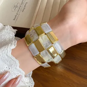 Bracciale a maglie quadrate in acrilico e oro indossato sul polso con pizzo elegante.