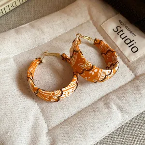 Detailed close-up showing the orange paisley fabric texture on bohemian hoop earrings